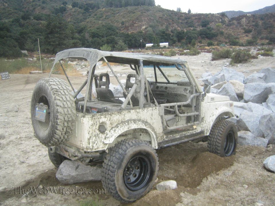 1987 Suzuki Samurai with roll cage and spare tire on rear, stuck in dirt and rocks