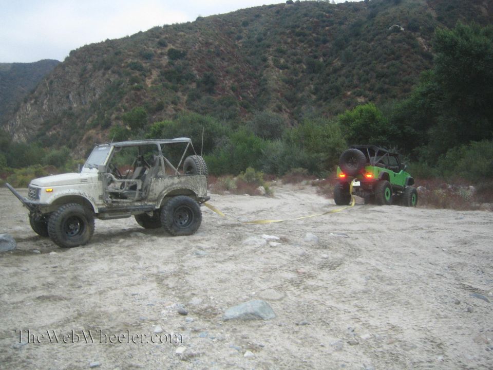 White Suzuki Samurai being towed by a green Jeep in a dry riverbed