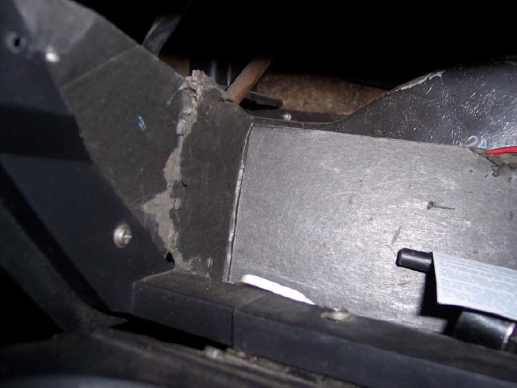 Under-dash view of gray heater duct and black plastic housing with screws and wiring