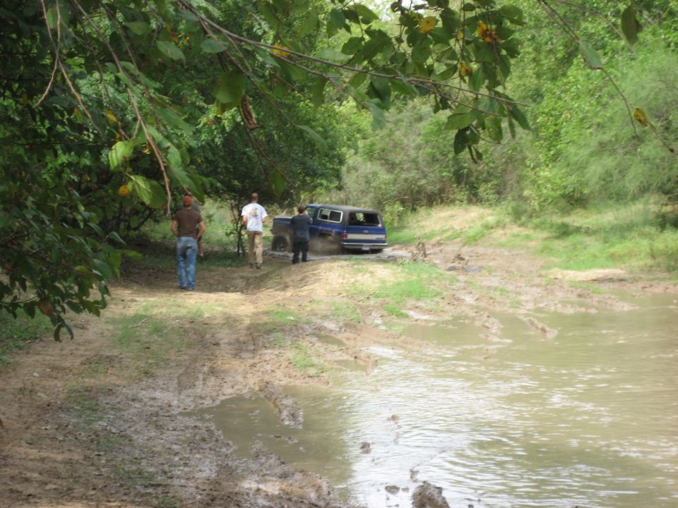 Blue SUV stuck in muddy water with people standing nearby