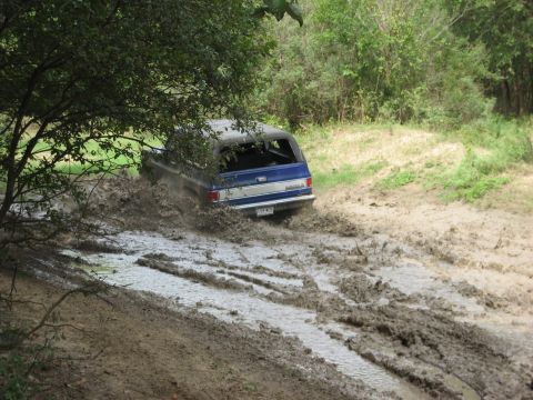 1986 Ford Bronco - This SUV is navigating a challenging muddy terrain, kicking up water and dirt.