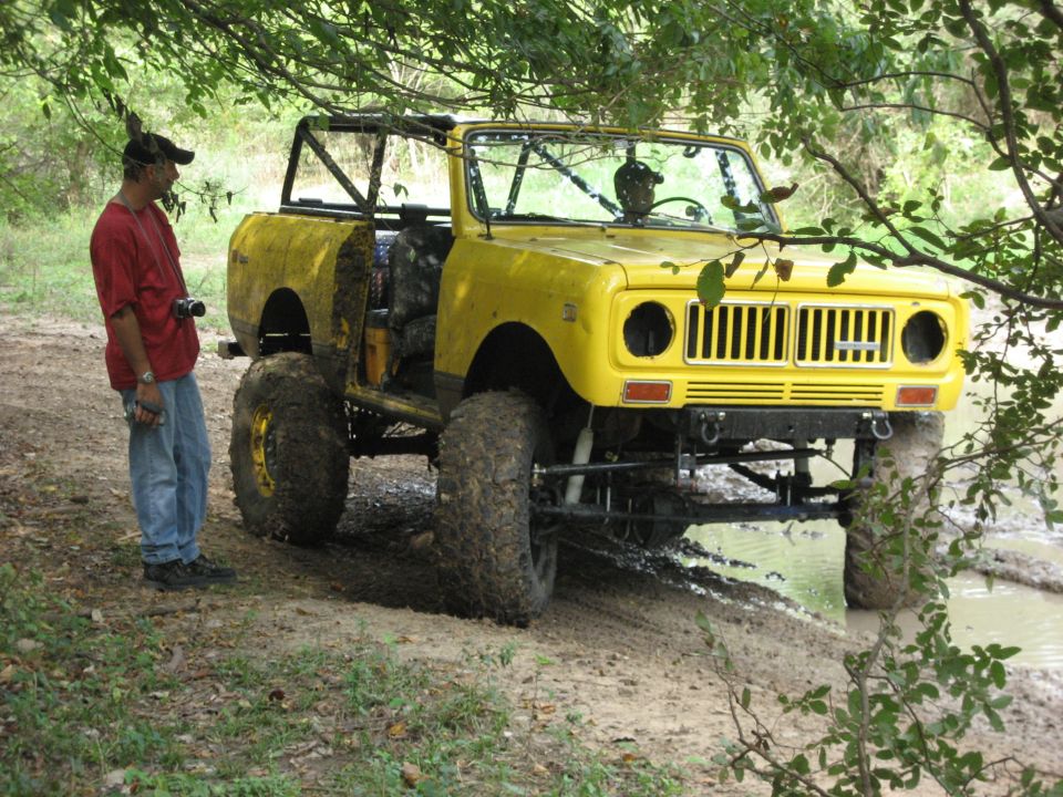 Yellow International Harvester Scout II off-road vehicle with large tires, modified roll cage, and a person standing next to it