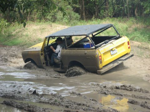 1986 Ford Bronco - An off-road vehicle navigates through a muddy terrain, with its tires deep in the mire.