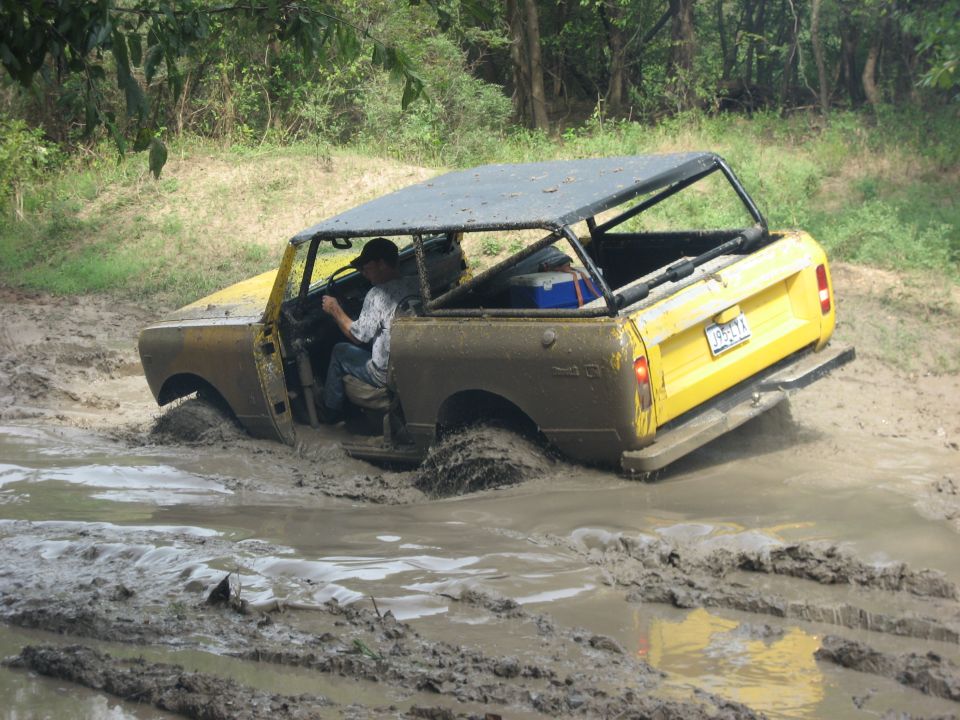 Yellow and brown off-road vehicle stuck in mud, driver visible, roof rack with cooler