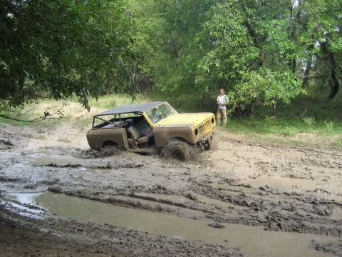 1986 Ford Bronco - This yellow off-road vehicle is deeply stuck in a muddy trail, with a person observing from the side.