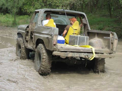 1986 Ford Bronco - This SUV is deep in the mud, with two occupants navigating the difficult terrain.