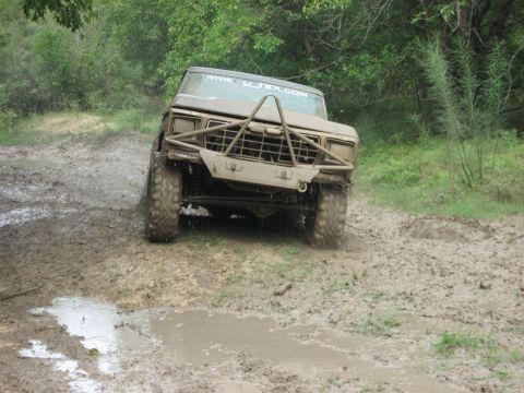 1986 Ford Bronco - A heavily modified 1980s Ford Bronco navigates a muddy off-road trail.