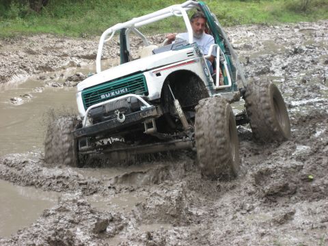 1986 Ford Bronco - A modified Suzuki Samurai navigates a muddy off-road course, kicking up water and mud.