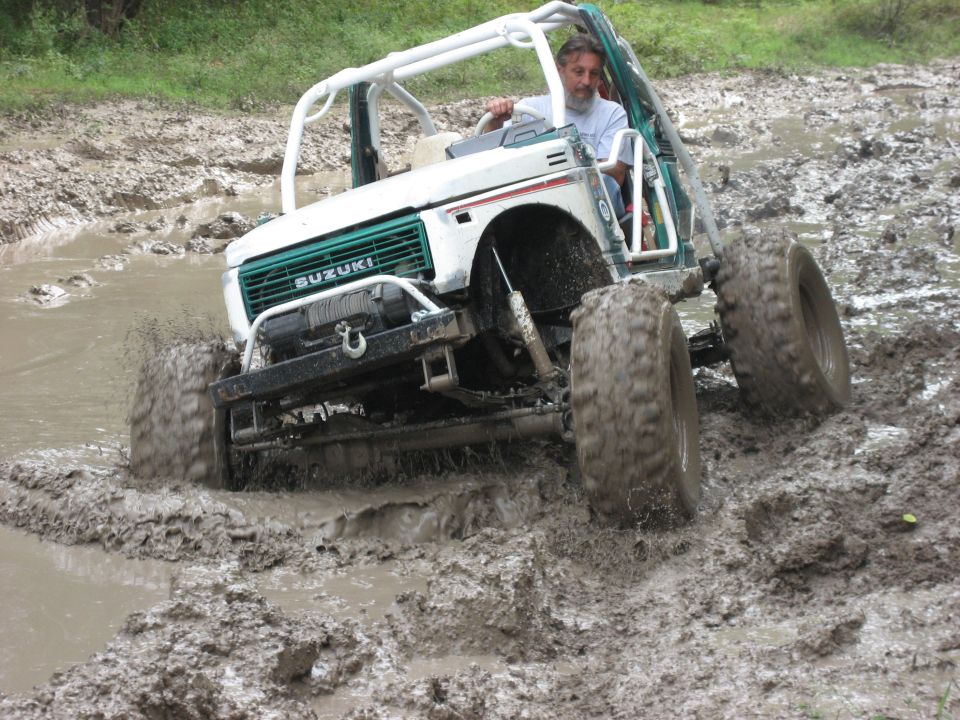 Suzuki Samurai driving through mud, white body, green grille, roll cage, large tires
