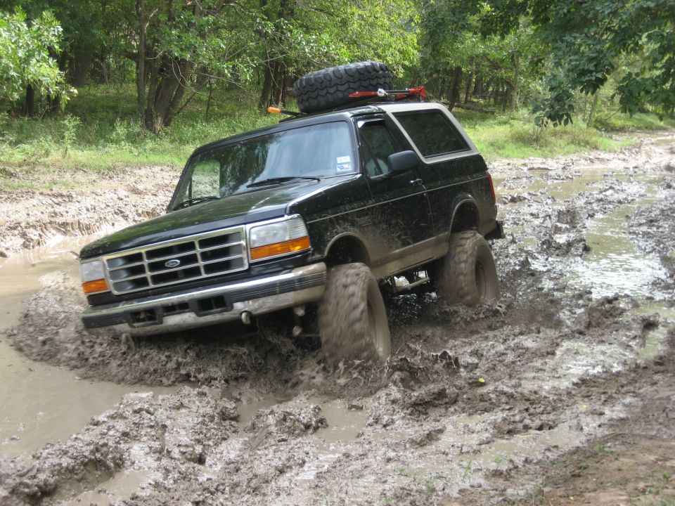 Black Ford Bronco driving through mud pit