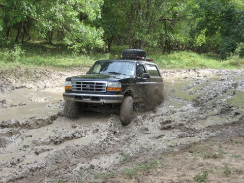 1986 Ford Bronco - Black Ford Bronco navigating a challenging muddy off-road course.