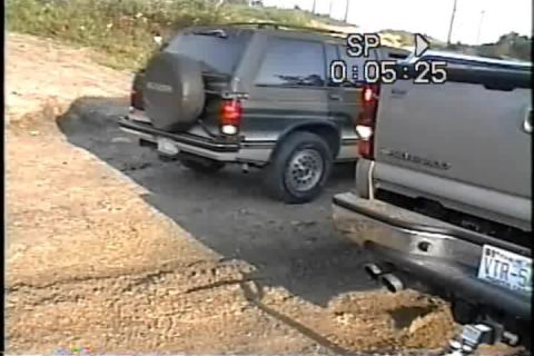 1989 Ford Bronco - A dark SUV with a spare tire mounted on its rear door is partially visible, alongside another vehicle.