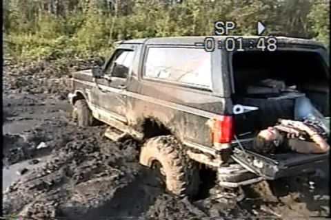 1989 Ford Bronco - Muddy 1989 Ford Bronco with tailgate open, stuck in a mire with a person resting inside the cargo area.