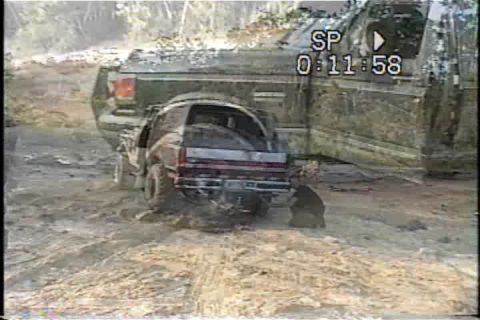 1989 Ford Bronco - Two off-road vehicles are stuck in the mud, with one appearing to be a truck and the other an SUV.