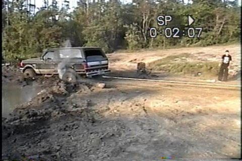 1989 Ford Bronco - A 1989 Ford Bronco is stuck in a muddy area, with smoke billowing from the front wheel.