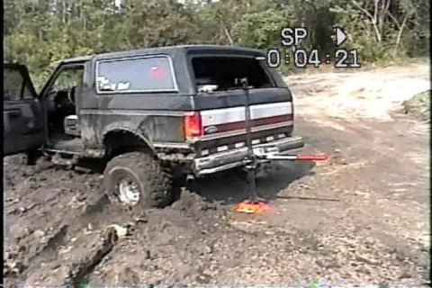 1989 Ford Bronco - This lifted Ford Bronco is deep in the mud, with its driver's side door open and a jack positioned under the rear.