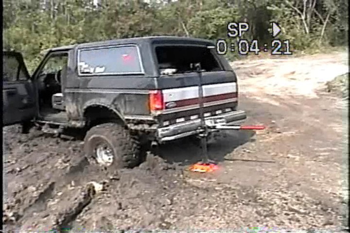 Black Ford Bronco with lifted suspension stuck in mud, jack under rear bumper