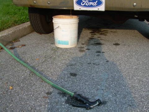 1988 Ford Bronco - A 1988 Ford Bronco is shown with a bucket placed to catch a leak from underneath the vehicle, with a green hose nearby.