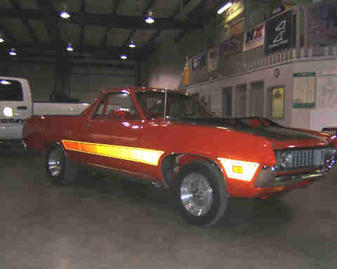 1967 Ford Ranchero - A red 1970 Ford Ranchero with a distinctive side stripe is parked indoors next to a white truck.