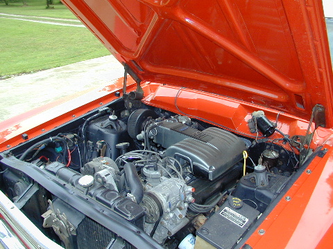 1967 Ford Ranchero - The engine bay of an orange vehicle is shown with the hood open, revealing the V8 engine and various components.