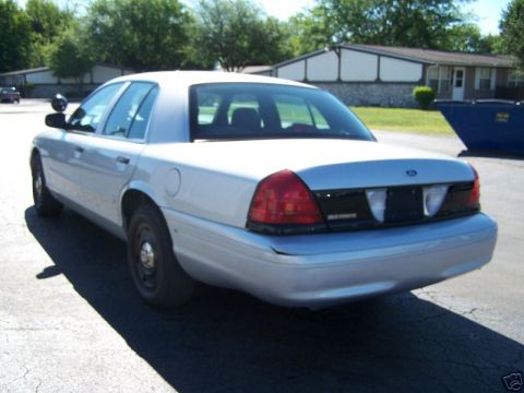 2003 Ford Crown Victoria - A silver 2003 Ford Crown Victoria sedan is parked on asphalt with a blue dumpster in the background.