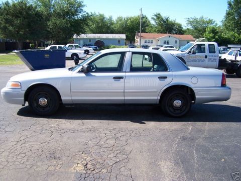2003 Ford Crown Victoria - Silver 2003 Ford Crown Victoria sedan parked outdoors with other vehicles and buildings in the background.