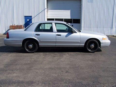 2003 Ford Crown Victoria - A silver 2003 Ford Crown Victoria sedan is parked outdoors in front of a large garage door.