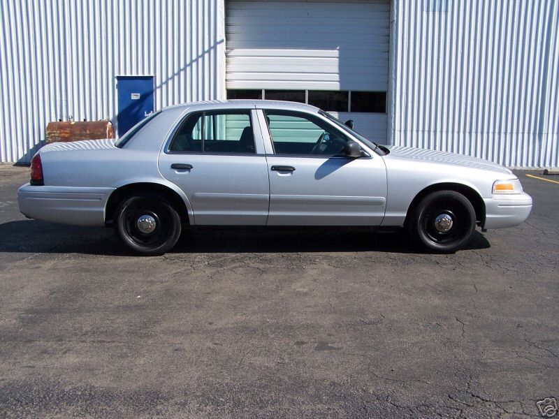 Silver 2003 Ford Crown Victoria sedan, side view, parked in front of a corrugated metal building