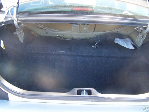 2003 Ford Crown Victoria - The interior of a car's trunk is shown, with dark carpeting and exposed wiring.