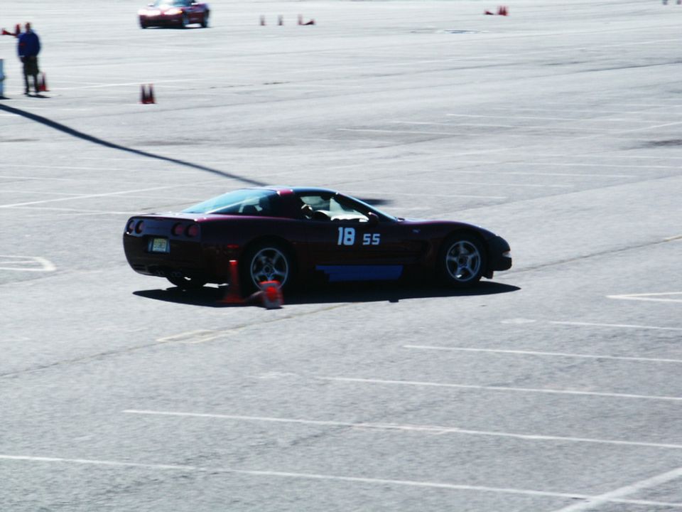 Dark red Chevrolet Corvette with number 18 SS on the door, on a race track with cones. Another car is visible in the background