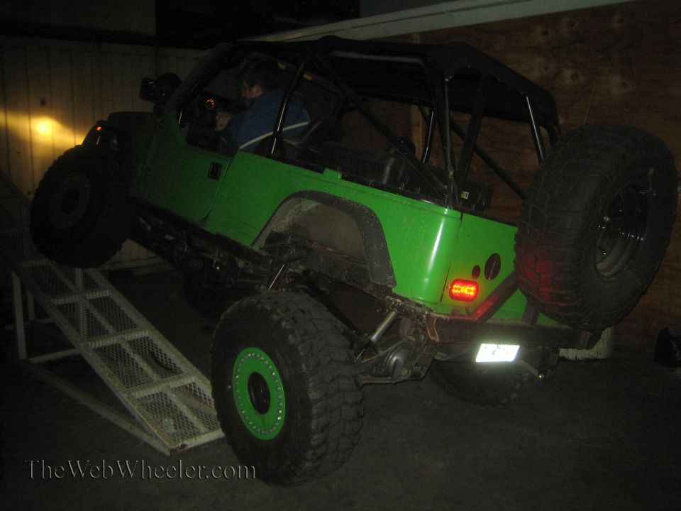Green off-road Jeep with large tires on a metal ramp, spare tire mounted on the back