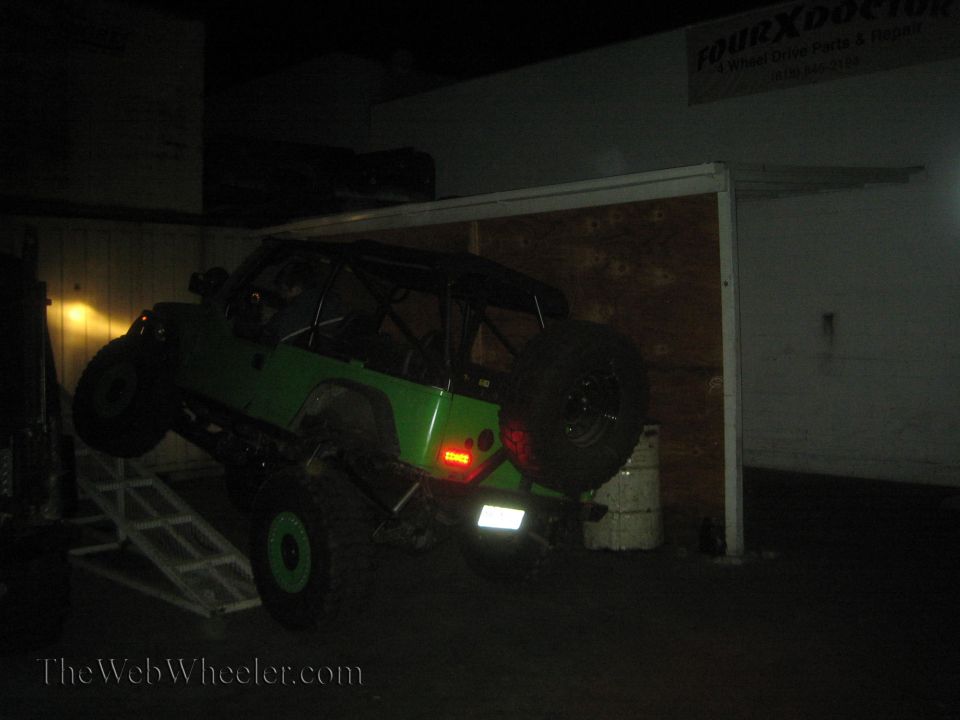 Green Jeep Wrangler on a ramp inside a garage, with a roll cage and spare tire visible