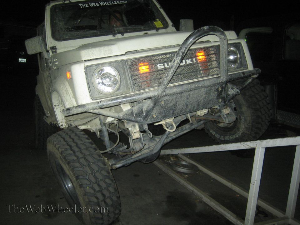 White Suzuki Samurai with aftermarket bumper on a ramp, front view