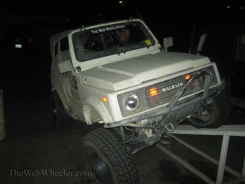 1987 Suzuki Samurai on a ramp, front grille says SUZUKI. The Web Wheeler.com sticker on windshield