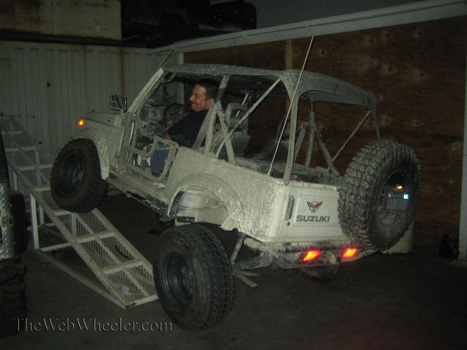 Suzuki Samurai on a ramp, covered in mud. Driver is visible