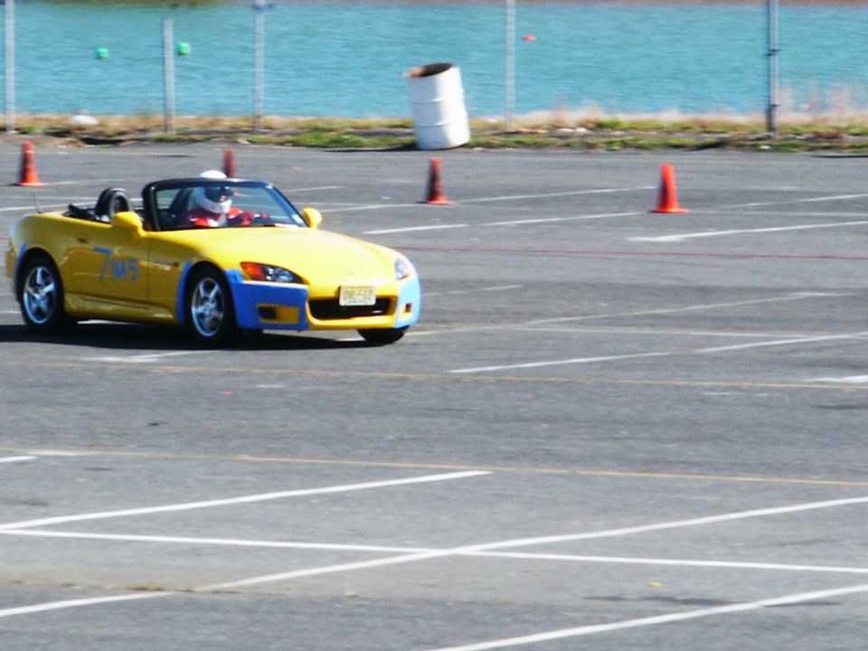 Yellow convertible sports car with blue front bumper and racing decals on a paved track with orange cones
