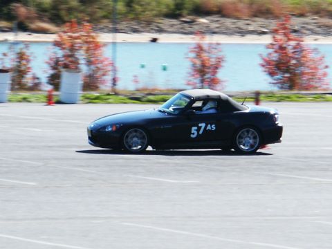 2001 Mercury Grand Marquis - A black convertible sports car with racing numbers is seen on a track with a body of water in the background.