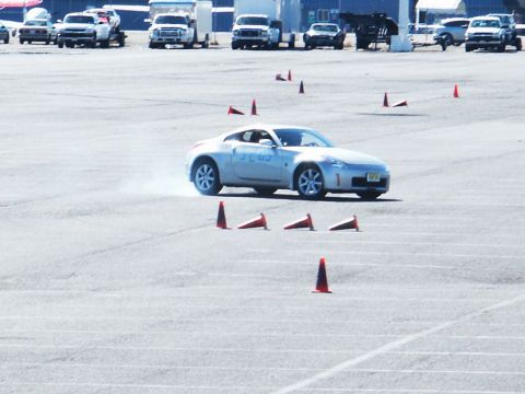 2001 Mercury Grand Marquis - A silver sports coupe is seen maneuvering through a cone course on a paved track, with other vehicles visible in the background.
