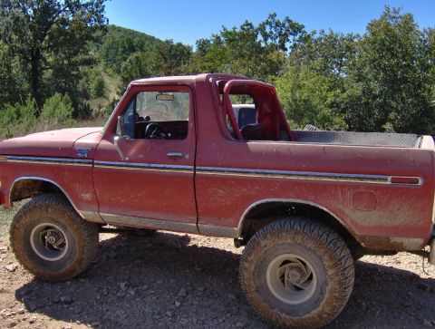 1978 Ford Bronco - A red 1978 Ford Bronco is parked on a dirt road with trees in the background.