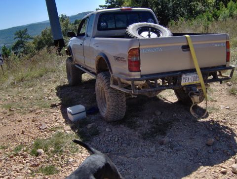 1978 Ford Bronco - Tan Toyota Tacoma pickup truck with aftermarket bumper and spare tire in bed, parked on gravel.