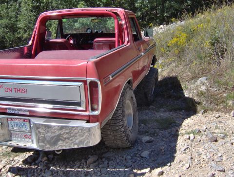 1978 Ford Bronco - Rear view of a red 1978 Ford Bronco parked on a dirt road with off-road tires.