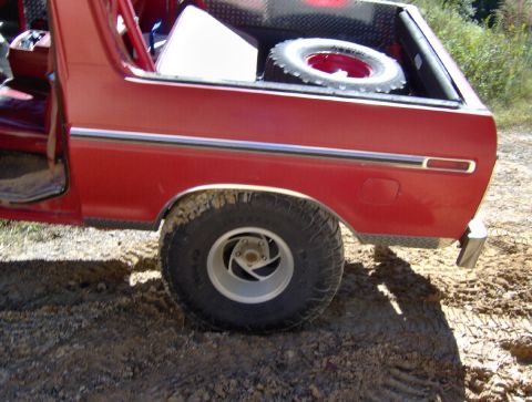 1978 Ford Bronco - Rear side view of a red 1978 Ford Bronco, showing diamond plate lining the bed and a spare tire.