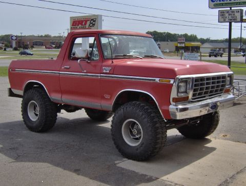 1978 Ford Bronco - A red Ford Bronco with large off-road tires is parked in front of a building with a sign for Italian restaurant.