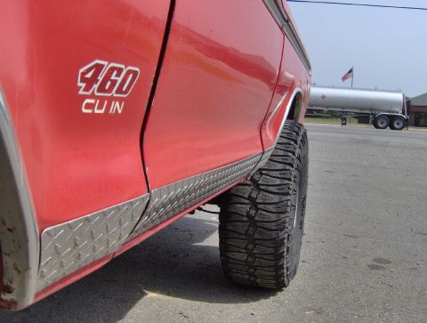 1978 Ford Bronco - Side view of a red SUV diamond plate trim and '460 CU IN' badging, with a tanker truck in the background.