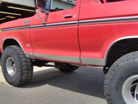 1978 Ford Bronco - Close-up of a red 1978 Ford Bronco's side, highlighting its diamond plate trim and off-road tires.