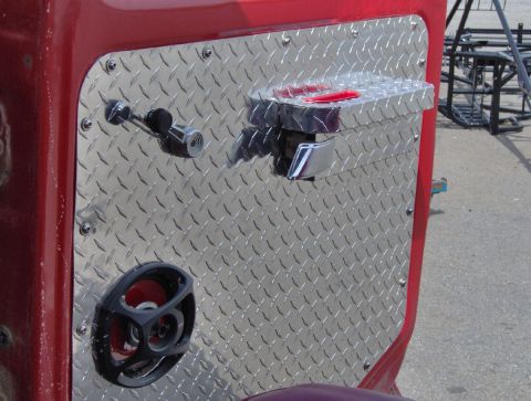 1978 Ford Bronco - Close-up of the inside of a red truck door skinned in polished aluminum diamond plate held on with exposed screws. A chrome interior door h…