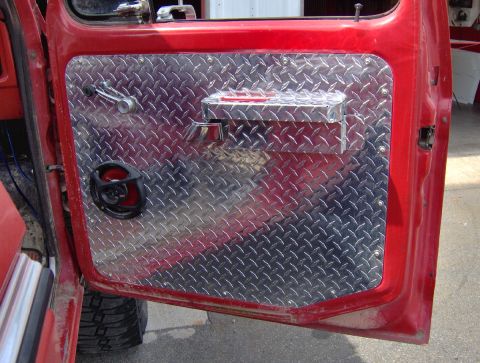 1978 Ford Bronco - Close-up of a red vehicle door interior a diamond plate panel and a speaker.
