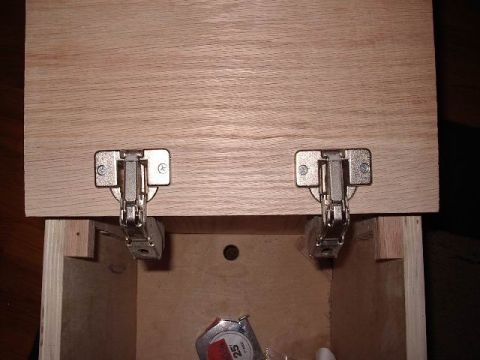 1985 Ford Bronco - Cabinet hinges installed on a wooden panel, with a tape measure visible below.