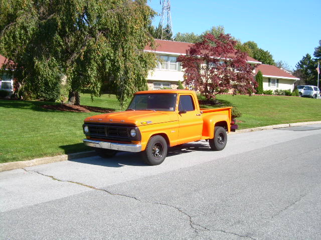 Orange Ford stepside pickup parked on a hilly residential street
