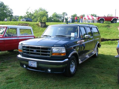 1995 Ford C-150 (Centurion Conversions) - A dark blue Ford Bronco SUV is parked on a grassy field next to a red Bronco and other vehicles.